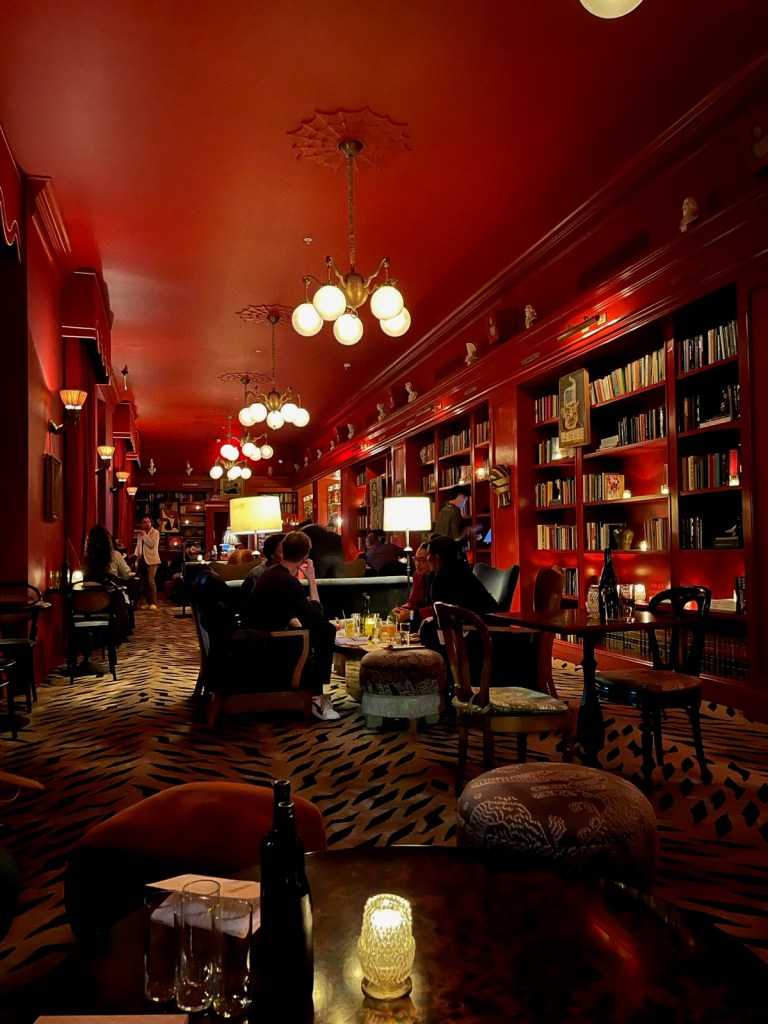 inside of bar marilou with red bookcases, ceiling, and victorian inspired chandeliers 